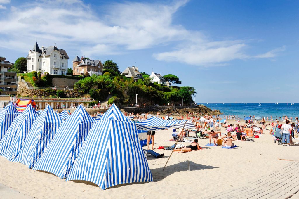 Dinard beach with blue and white striped tents overlook by large villas on the cliff above