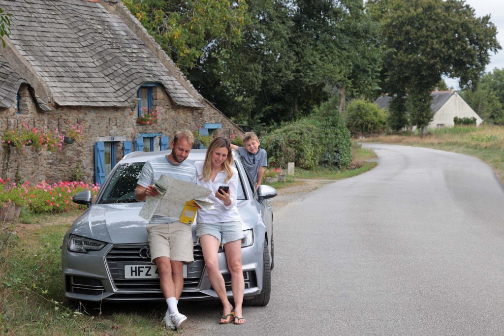 Family sat on front of car with a map, driving in France from St Malo